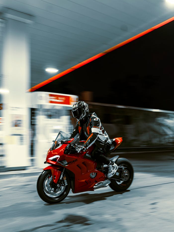 our-story A motorcyclist speeds through a gas station at night on a red Ducati, capturing the thrill of motion and adventure.