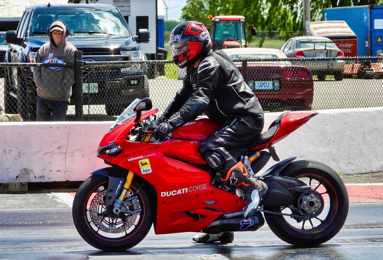 about-us A motorcyclist in full gear races a red Ducati on a sunny day in Cayuga, Ontario.